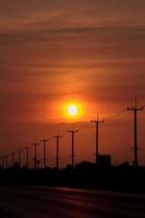 Atmósfera en el poste de alto voltaje de la tarde al lado de la carretera y el cielo anaranjado. El gran sol que se estaba poniendo era hermoso cuando estaba de camino a casa, era una hermosa atmósfera romántica. foto