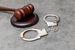 Law theme. Court of law trial in session. Judge gavel handcuffs on grey table in lawyer office or court session. Mallet of judge on concrete stone grey background. Justice human rights concept. photo