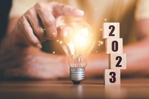 concepto de inicio de año nuevo 2023, concepto con innovación e inspiración, tecnología innovadora en concepto científico y desarrollo empresarial moderno, idea creativa, bloques de madera y bombillas en la mesa foto