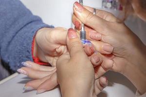 tratamiento para el cuidado de las manos: el manicurista quita el esmalte de uñas de un dedo femenino. foto
