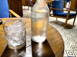 refrescante vodka frío en la botella con rocas de hielo en el vaso servido en el pub foto