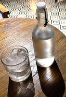 refreshing cold vodka in the bottle with ice rocks in the glass served in the pub photo