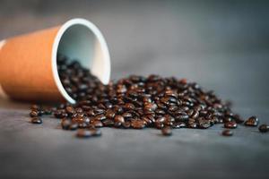 los granos de café se dispersan de una taza de papel marrón. foto