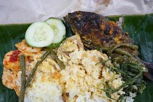 rice wrapped in grilled fish, cucumber, long beans, sweet potato shoots, jackfruit, and crackers photo