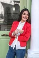 Woman standing at wall holding cup in hands photo