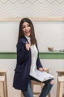 Woman with clipboard pointing at camera in cafe photo