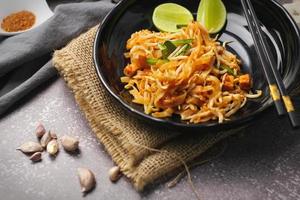 Pad Thai or Thai-style pad Thai served with lime and seasonings In a black plate, it's a food that can be found in street food in Thailand. photo