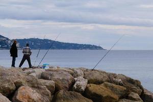 Men are fishing on the rocks in the sea outdoors in Nice, France. photo