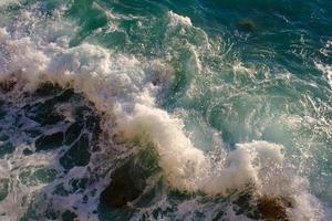 roca rompiendo con agua de mar, al aire libre, olas y rocas, salpicaduras y espuma, vista superior. foto
