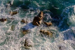 Water flowing into the sea, outdoors, waves and stones, splash and foam, top view.