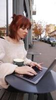 mulher sentada do lado de fora em uma cafeteria com laptop video