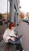 Woman seated outside at coffee shop with laptop video