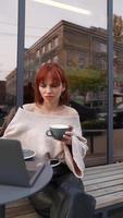 Woman seated outside at coffee shop with laptop video