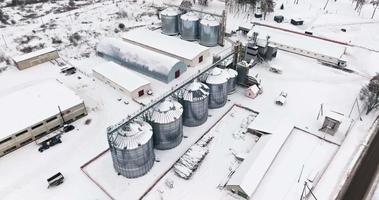 vuelo sobre el elevador de granero de agro silos en día de invierno en campo nevado. silos en la planta de fabricación de procesamiento agrícola para el procesamiento, secado, limpieza y almacenamiento de productos agrícolas video