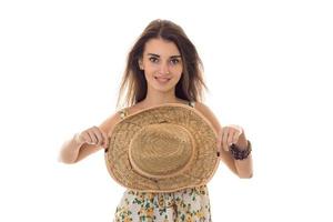 young pretty brunette girl in sarafan with floral pattern and straw hat with wide brim smiling on camera isolated on white background photo