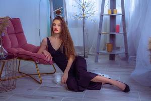 portrait of Glamour lady with red lips in black overalls sits on the floor at home photo