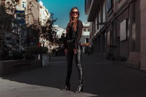 retrato de dama glamurosa con traje de cuero y gafas de sol mirando hacia otro lado en la calle foto