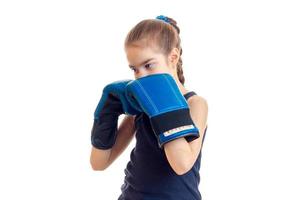 little girl with pigtail stands in the large blue boxing gloves in front of a camera photo