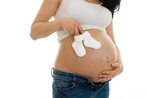 young pregnant woman posing in white shirt with little socks in her hands isolated on  background photo