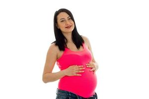 young pregnant brunette woman with big belly posing in pink shirt isolated on white background photo