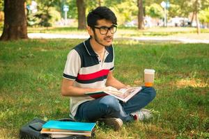 young student sitting on a lawn with coffee and books photo