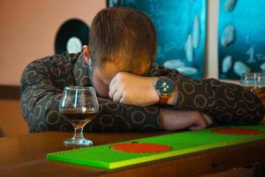 borracho durmiendo en la mesa del bar cerca de una copa de brandy foto