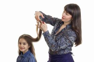 woman makes a hairstyle a little girl isolated on a white background photo