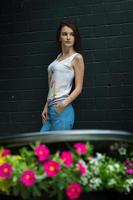 beautiful tender brunette stands near the pink flowers and dark walls outdoors photo