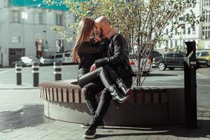 retrato de una pareja alegre enamorada sentada en un banco y riendo en la calle foto