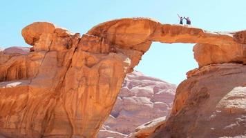 Arabisch bedoeïenen gids met toerist staan houding Aan beroemd boog brug in wadi rum woestijn houding en genieten panoramisch visie van toneel- rots formaties video