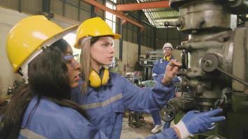 ein industriearbeiterteam in schutz- und sicherheitsuniformen und helmen, ein männlicher manager und weibliche kollegen arbeiten mit metallbearbeitungsmaschinen in der fertigungsfabrik. professioneller Produktionsingenieur. video