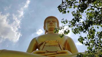 vista frontal estátua de buda grande dourada phra buddha dhammakaya thep mongkol no templo wat pak nam phasi charoen. céu de luz solar e fundo de nuvens video