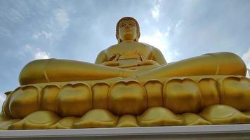 front view Golden big Buddha statue Phra Buddha Dhammakaya Thep Mongkol in Wat Pak Nam Phasi Charoen temple. Sunlight sky and cloud background video