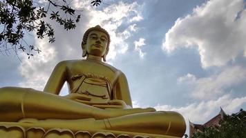 frontansicht goldene große buddha-statue phra buddha dhammakaya thep mongkol im wat pak nam phasi charoen tempel. sonnenlicht, himmel und wolkenhintergrund video