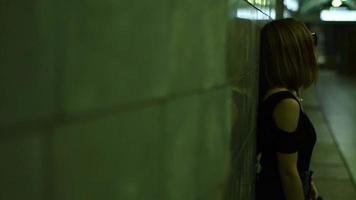 young lonely girl in black glasses and t shirt stands in an underpass near a wall video