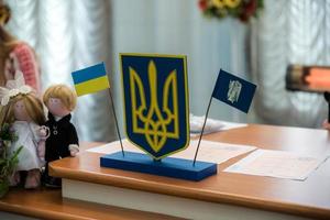 bandera ucraniana y escudo de armas con tela con textura de camuflaje pixelado. tela con patrón de camuflaje en formas de píxeles grises, marrones y verdes con el signo tridente ucraniano en la oficina de registro foto