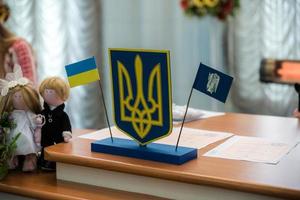 Ukrainian flag and coat of arms with fabric with texture of pixeled camouflage. Cloth with camo pattern in grey, brown and green pixel shapes with Ukrainian trident sign in the registry office photo