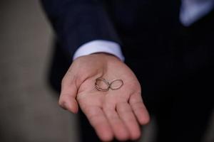 novio con anillos de boda en la mano. dos anillos de boda en el suelo con anillos de boda en contraste en el suelo, en el suelo, en el piano, en la mano foto