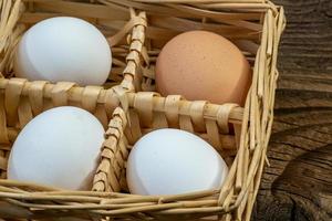 huevos de gallina en una cesta de mimbre sobre una antigua mesa de madera entablonada. Bodegón de cocina rural. foto