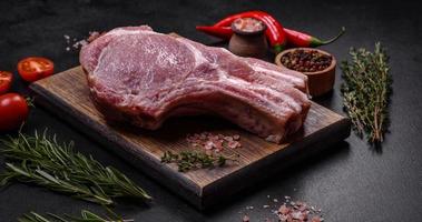 carne de cerdo cruda fresca en las costillas con especias y hierbas en una tabla de cortar de madera foto