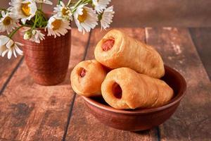 Homemade sausages in dough in a clay plate on a dark background, fast food photo