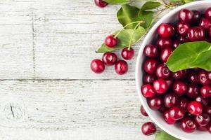 Fresh sweet cherries white bowl with leaves in water drops on wooden background
