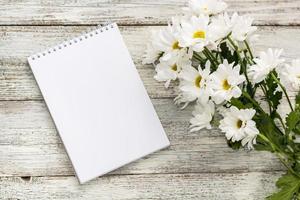 spring bouquet of white daisies with clean notebook to write on white wooden table