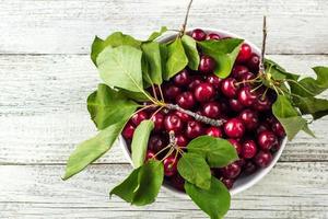 Fresh sweet cherries white bowl with leaves in water drops on wooden background photo