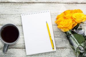 Notepad and tea with a bouquet of yellow roses on a white wooden background photo