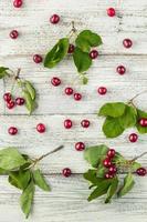 Red ripe cherry berries and green leaves on white wooden background. top view photo