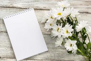 spring bouquet of white daisies with clean notebook to write on white wooden table photo