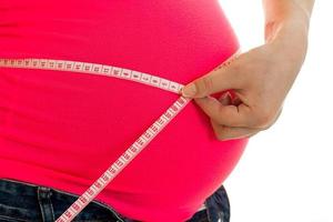El primer plano de una mujer embarazada mide su gran barriga con cinta aislada de fondo blanco foto