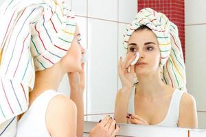 girl with a big towel on her head looks in the mirror and rubs face with a cotton disk photo