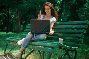 smiling lady sitting on a bench and looking at laptop photo